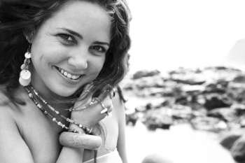 Young adult Caucasian female smiling at viewer holding necklace.