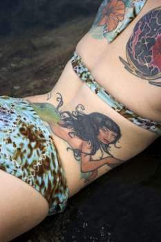 Sexy tattooed Caucasian woman in bikini lying in tidal pool in Maui, Hawaii, USA.