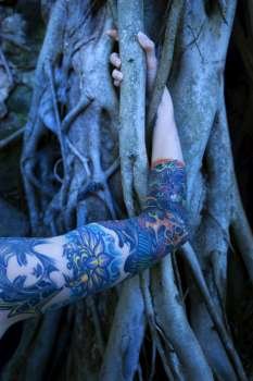 Blue-toned portrait of tattooed Caucasian woman´s arm intertwined with Banyan tree in Maui, Hawaii, USA.