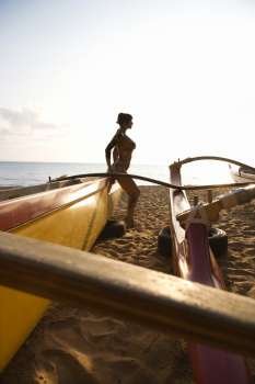 Silhouette of sexy Caucasian woman in bikini beside outrigger canoe on beach in Maui, Hawaii, USA.