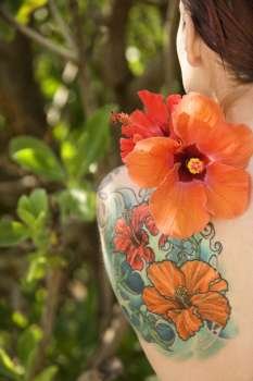 Back view of tattooed Caucasian woman with Hibiscus flower over her shoulder in Maui, Hawaii, USA.