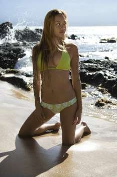 Sexy young adult Asian Filipino female kneeling on beach in bikini in Maui Hawaii.