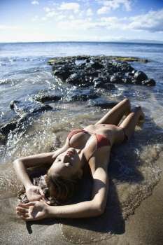Young adult Asian Filipino female lying on beach in bikini in Maui Hawaii.