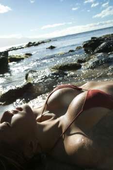 Breast shot of young adult Asian Filipino female lying on beach in bikini.