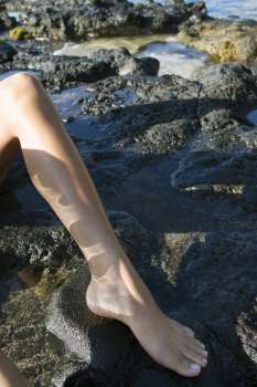 Leg and foot of young adult Asian Filipino female on rocks on beach in Maui Hawaii.