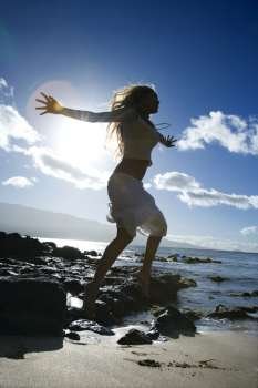 Young adult Asian Filipino female jumping on beach in Maui Hawaii.