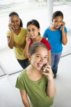 Preteen girls of mutiple ethnicities talking on cell phones and looking at viewer.
