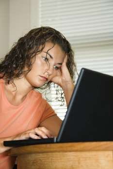 Pretty young adult Caucasian brunette woman sitting and working on laptap computer.