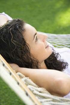 Side view of pretty young adult Caucasian brunette female lying in hammock smiling.