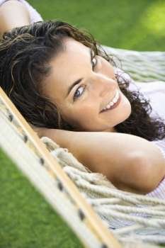 Portrait of pretty young adult Caucasian brunette female lying in hammock smiling up at viewer.