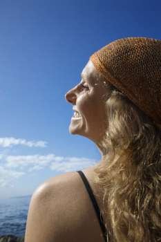 Profile of smiling Caucasian mid-adult woman with wavy hair and head scarf at coast.