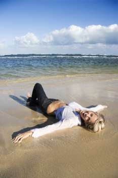 Pretty Caucasian woman lying on water´s edge on beach in Maui, Hawaii smiling.