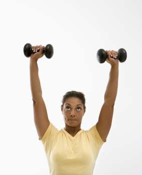 Mid adult multiethnic woman holding dumbbells over head with determined look on her face.