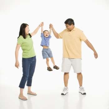 Asian mother and father holding hands with son and lifting him up in front of white background.