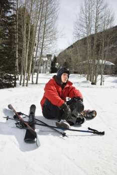 Caucasian male teenager sitting on snow with ski gear.