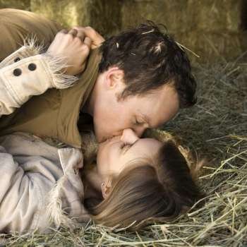Young adult Caucasian couple lying down in hay kissing.