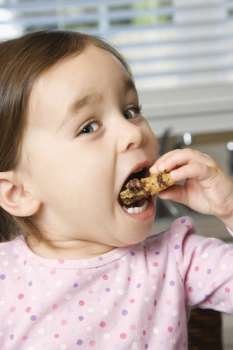 Caucasian girl eating chocolate chip cookie.