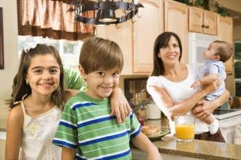 Hispanic mother and children smiling at viewer in kitchen.