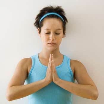 Young woman holding hands in prayer position with eyes closed meditating.