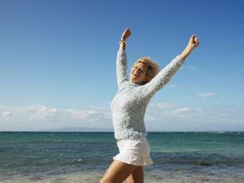 Portrait of attractive young blond woman smiling with arms raised in air on Maui, Hawaii beach.
