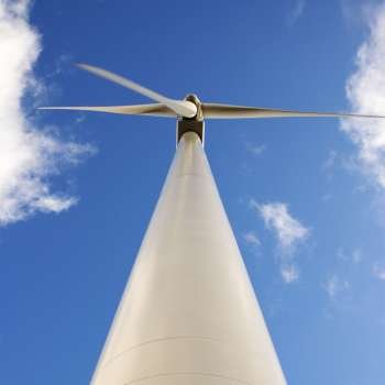 Perspective shot of wind turbine against blue sky.