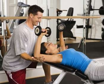 Man assisting woman at gym with hand weights smiling.