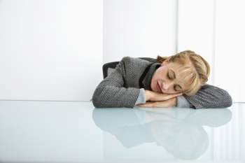 Caucasian woman sleeping on desk with head on hands.