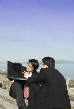 Two businessmen working together with their laptop on the beach
