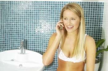 20s attractive woman in her bathroom wearing white lingerie talking on her mobile phone.