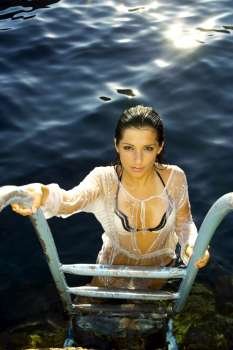 A stock photograph of a beautiful young woman posing on a ladder by the water in Malta.