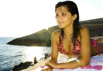 A stock photograph of an attractive young model relaxing on her towel by the sea in Malta.