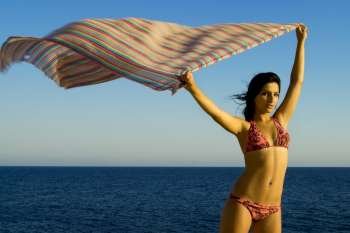 A stock photograph of a free young woman holding her sarong into the breeze,