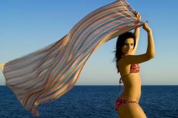 A stock photograph of a free young woman holding her sarong into the breeze,