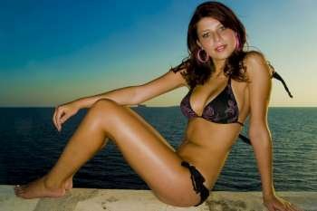 A stock photograph of a happy young model wearing a black bikini by the sea during a beautiful sunset.