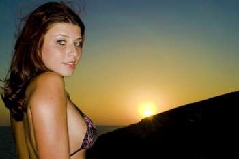 A stock photograph of a happy young model wearing a black bikini by the sea during a beautiful sunset.