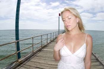 A stock photograph of a blonde woman relaxing by the beach in a white dress.