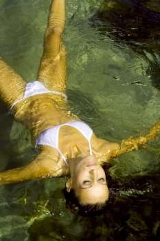 A stock photograph of a beautiful young woman relaxing in a white bikini floating in the water.