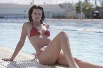 A stock Photograph of a young model sitting by a pool in her red bikini.