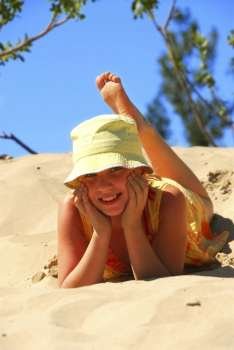 Young girl in yellow hat lying on top of a sand dune