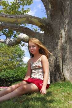 Young girl sitting under old big tree in the summer