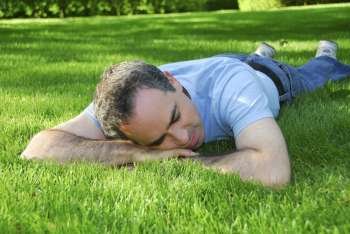 Attractive man lying on green grass in a park relaxing