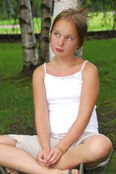 Portrait of a young pretty girl sitting under a birch tree in a park