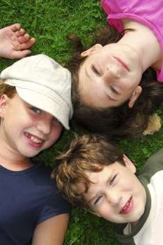 Portrait of three young children lying on grass looking up