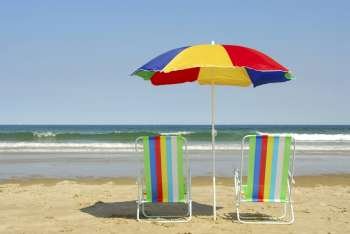 Beach chairs and umbrella on the ocean shore with surf in the background, horisontal