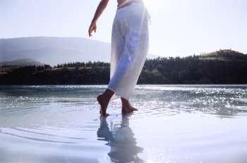 Woman´s legs outdoors walking on water in scenic location (lens flare)
