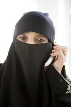 Woman indoors on cellular phone wearing veil (high key)
