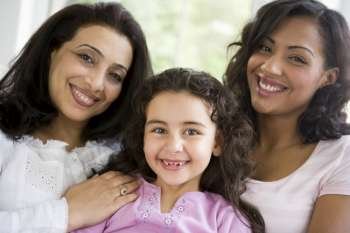 Two women and young girl in living room embracing and smiling (high key)