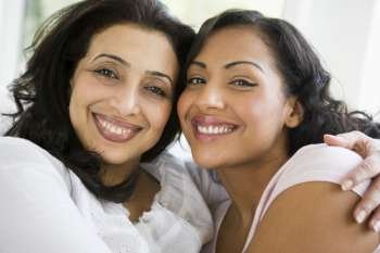 Two women in living room embracing and smiling (high key)