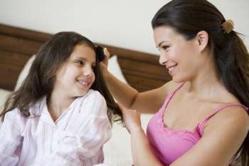 Woman brushing young girl´s hair on bed in bedroom smiling (selective focus)