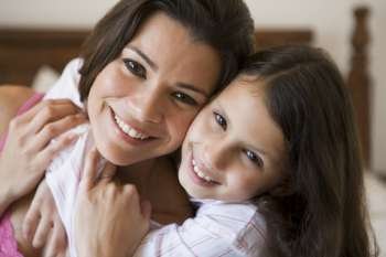 Woman and young girl in bedroom embracing and smiling (selective focus)